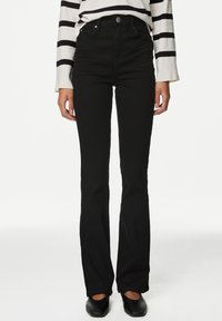 Pantalones vaqueros negros de campana con una cintura alta, hechos de denim, que cuentan con bolsillos frontales y cierre de botones. Combinados con una blusa a rayas en blanco y negro.