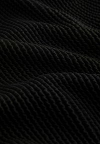 Gros plan sur un tissu noir avec une texture nervurée ondulée en relief créant des plis doux et fluides ainsi que des ombres.