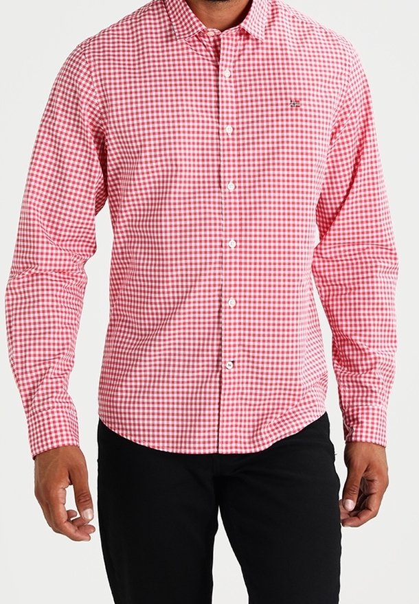 Homme portant une chemise à carreaux rouge et blanche boutonnée à manches longues et un pantalon noir, debout les bras détendus le long du corps.