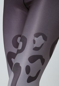 Högmidjade leggings i grått med ett slätt, stretchigt tyg. Har ett svart abstrakt mönster som framhäver benens form och design.