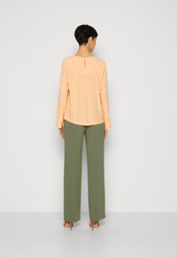 Blouse fleurie pêche à manches longues avec détail en forme de trou de serrure au dos, associée à un pantalon large taille haute vert et des sandales à talons beiges.