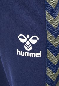 Marineblaue Sporthosen mit einem weißen Logo und strukturierten grünen seitlichen Akzenten im Zickzackmuster. Aus weichem Stoff gefertigt für zusätzlichen Komfort.
