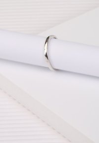 Silver ring with a smooth, polished finish, rounded design, and reflective surface, resting on a white cylindrical object.