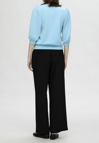 Suéter de manga abullonada azul claro, de tela suave, combinado con pantalones de pierna ancha negros de talle alto, usados con zapatos negros planos.