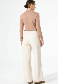 Beige Langarmoberteil mit subtiler Glanzoptik, kombiniert mit cremefarbenen Hosen mit elastischem Bund, von hinten gezeigt.