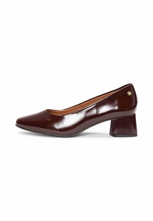 Zapato de mujer marrón oscuro brillante con tacón bajo de bloque, puntera redondeada y pequeño logo metálico cerca del talón sobre fondo blanco.