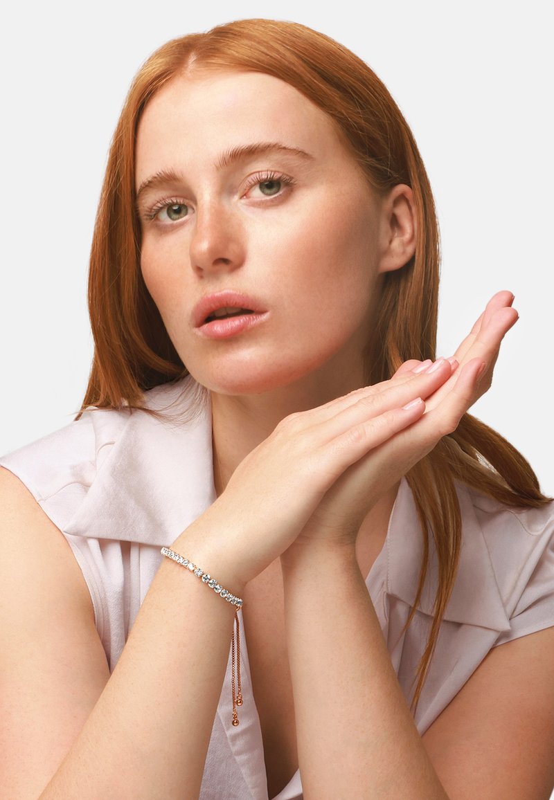 Sølvarmbånd med klare edelstener, med en delikat kjede. Modellen poserer med hendene sammen, og viser frem armbåndets design.