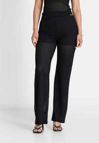 Zwarte gebreide wijd-uitlopende broek met een gestructureerd meshpatroon, hoge taille en een decoratieve gouden accenten op de tailleband.