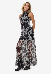 Rochie maxi cu imprimeu de vacă alb-negru, cu guler înalt, textură transparentă și un corset ajustat, asortată cu cizme negre până la gleznă.