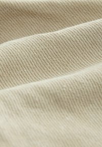 Tissu beige avec une surface texturée, présentant de fines crêtes et une légère duveteux, créant une apparence douce et durable.