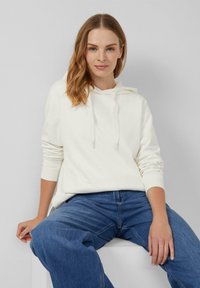 Bluza z kapturem w kolorze białym z bawełny, z kieszenią typu kangur, sznurkiem w kapturze i ściągaczami na rękawach, w zestawie z niebieskimi dżinsami.