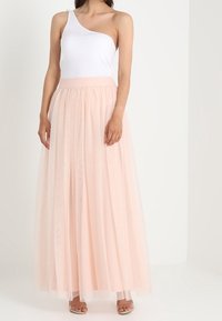 Eén-schouder witte top met een blushroze tule maxirok met een gathered tailleband en gelaagde doorschijnende stof. Simpele sandalen.