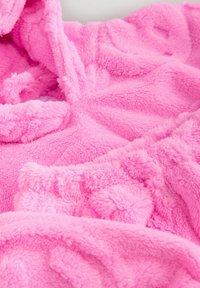 Pink fleece-tæppe med en blød, struktureret overflade og et plysset og fluffet udseende, designet til varme og komfort.