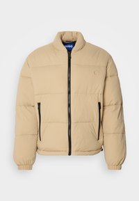 Jachetă puffer bej cu guler înalt, fermoar frontal și două buzunare cu fermoar. Dispune de un model matlasat și manșete elastice. Logo pe piept.