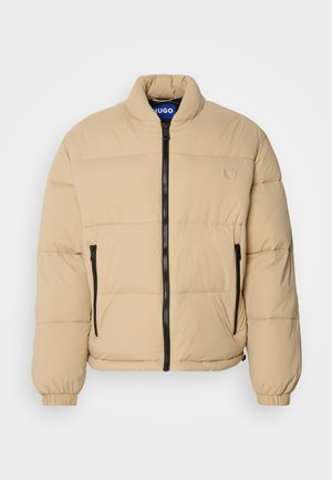 Beige puffer jacket with a high collar, zip front, and two zipped pockets. Features quilted pattern and elastic cuffs. Logo on the chest.