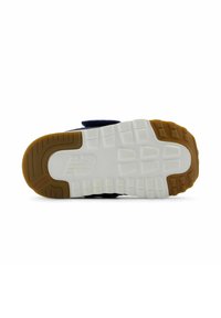 Suela de zapatilla deportiva con una base blanca texturizada, detalles de goma marrón y dibujos en la suela para agarre. Detalle de tiras de velcro visible.