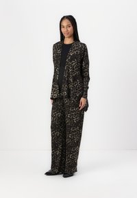 Svart och brun leopardmönstrad outfit med en lång kappa och vida byxor, tillverkad av ett mjukt tyg med en slät textur och avslappnad passform.