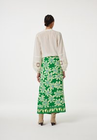 Geborduurde rok met groen bloemenpatroon, volle lengte. Witte blouse met ballonnenmouwen en kantafwerking. Beige hakken.