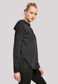 Schwarzer Hoodie mit lockerer Passform, seitlichen Schlitzen, strukturiertem Stoff und verstellbarem Kordelzug. Lange Ärmel und eine Kängurutasche sind ebenfalls enthalten.