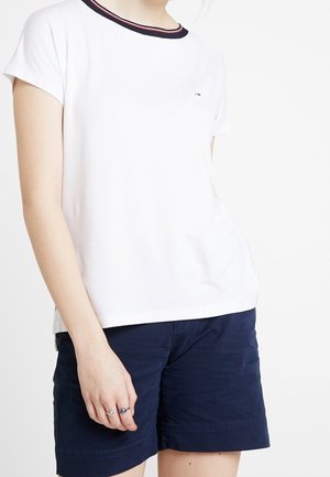 Witte t-shirt met korte mouwen en een ronde halslijn, voorzien van marineblauwe en rode gestreepte accenten. Gecombineerd met marineblauwe shorts, met een minimale textuur.