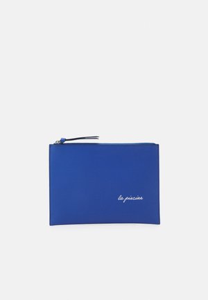 Blauwe ritszak gemaakt van een glad materiaal, met een minimalistisch ontwerp. Toont "la piscine" in witte schrift in de rechterbenedenhoek.