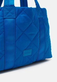 Vadderad blå tote-väska i nylon med textilhänken och rektangulär form. Har en märkesetikett och kontrasterande sidband.