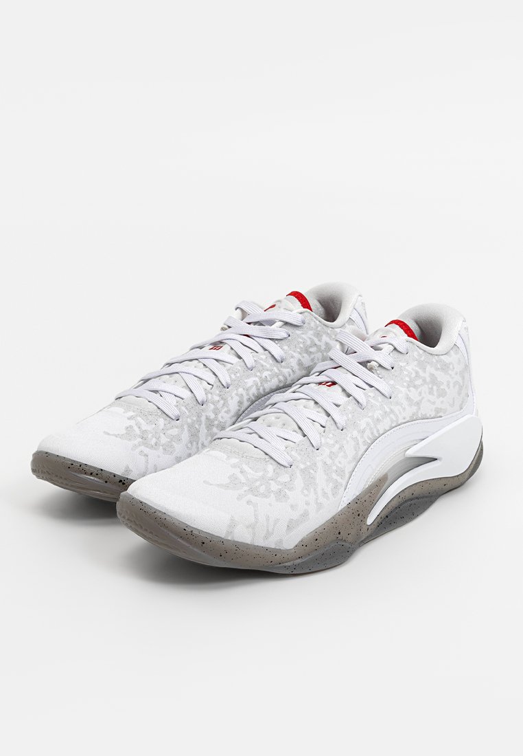 Weiße Sportschuhe mit strukturiertem Obermaterial, grau gesprenkelter Sohle und roten Akzenten an der Zunge. Sie verfügen über eine traditionelle Schnürung und ein glattes Design.