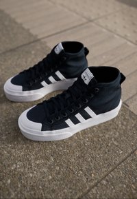 Sneakers alte in tela blu navy con suola in gomma bianca e tre strisce bianche. Presentano una parte superiore testurizzata e chiusura con lacci.