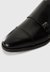Schwarze Lederdressschuhe mit glatter Oberfläche, spitzer Zehenform, doppelter Schnallengestaltung und subtilen Nahtdetails entlang der Kante.