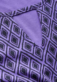 Violetti vaate, jossa on musta timanttimalli. Yläosassa on avaus kaula-aukossa, joka näyttää sileältä kankaalta.