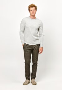 Helles graues Langarmshirt kombiniert mit strukturierten, dunkelbraunen tapered Hosen und beigen Sneakers. Das Outfit ist figurbetont und lässig.