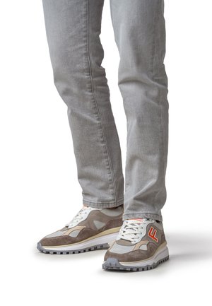 Baskets combinant des matériaux gris et beige, avec une superposition en daim texturé, des côtés en mesh et un logo bien visible en rouge.