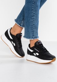 Czarne skórzane sneakersy z białymi akcentami, sznurowanym fasonem i masywną białą podeszwą. Gumowa podeszwa zewnętrzna zapewnia przyczepność. Logo na języku.