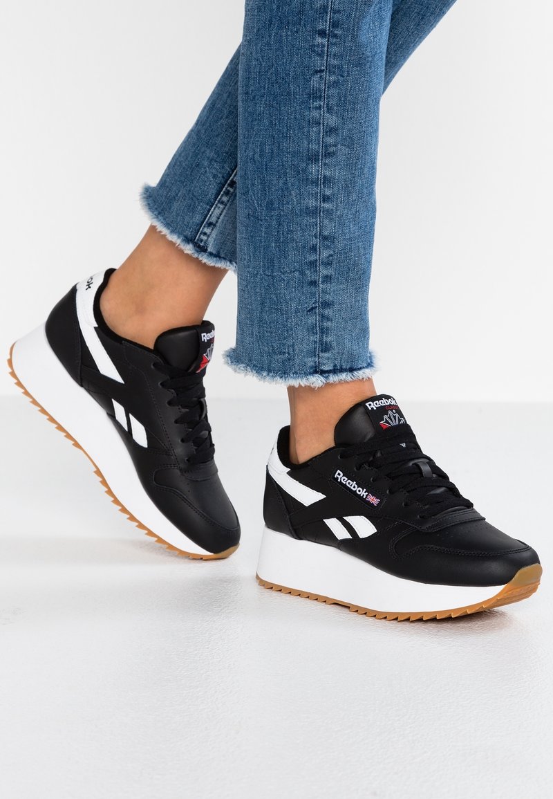 Czarne skórzane sneakersy z białymi akcentami, sznurowanym fasonem i masywną białą podeszwą. Gumowa podeszwa zewnętrzna zapewnia przyczepność. Logo na języku.