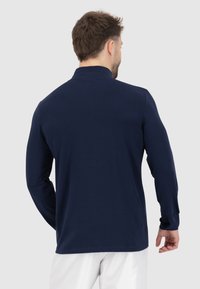 Polo a maniche lunghe di colore blu navy in cotone, con design semplice, colletto leggero e forma aderente. Texture liscia.