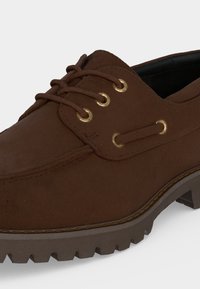 Chaussure en cuir marron à lacets avec semelle robuste et œillets dorés, conçue pour un usage décontracté ou en extérieur.