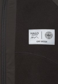 Sort fleecejakke med et sølvmærke. Har en frontlynlås og syninger, der viser "HALO" og "OFF PITCH" med et rundt logo.