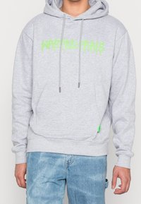 Felpa grigia con cappuccio, grande testo verde "WASTED PARIS," stringhe, e tasca frontale. Presenta polsini a coste e un'etichetta sul lato.