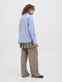 Hellblau-weißer gestreifter Langarmshirt, getragen mit beigen gefalteten Hosen und schwarzen Schuhen. Glatte Stofftextur.