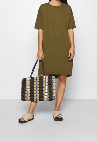 Oliwkowa sukienka w kształcie T-shirtu, oversize. Pleciona torba w paski czarno-biało-karmelowa z krótkimi uchwytami. Jasnobeżowe klapki.