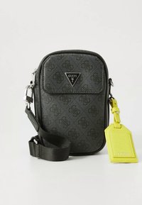 Kompakte schwarze Umhängetasche mit geprägtem Muster, verstellbarem Riemen, vorderer Tasche und einem gelben Etikett. Verfügt über ein dreieckiges Logo-Detail.