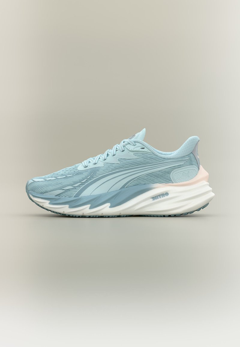 Baskets de sport bleu clair avec dessus texturé, semelle épaisse et ondulée blanche et bleue, et subtil accent rose au talon sur fond neutre.