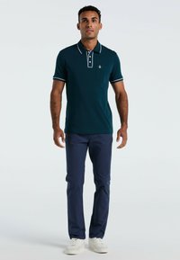 Polo bleu canard avec un col contrasté blanc et des accents blancs aux manches, avec une poche poitrine. Assorti à un pantalon navy et des baskets blanches.