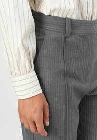 Gray pinstriped trousers made of smooth fabric, with a fitted waist and sharp creases. The cuffed sleeve features thin vertical stripes.
