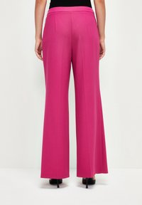 Růžové kalhoty s širokými nohavicemi z hladkého materiálu, s vysokým pasem a jemnými záhyby. Nabízejí rovný siluetu, která dosahuje k podlaze.