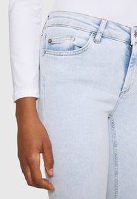 Jeans de mezclilla azul claro con un corte ajustado, que cuentan con un bolsillo frontal, cierre de botón y un ligero desvanecimiento. La tela tiene una textura suave.