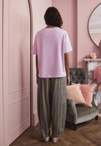 Pink cotton t-shirt with short sleeves, paired with wide-leg pants featuring vertical blue, green, and yellow stripes. Textured backdrop.
