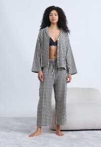 Σετ ρούχων άνεσης με ασπρόμαυρο καρό σχέδιο, που περιλαμβάνει κοντό σακάκι και φαρδιά παντελόνια. Μαλακό ύφασμα με χαλαρή γραμμή.