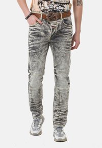 Verblasste graue Jeans mit einem abgenutzten Look, die über einzigartige Nahtdetails, mehrere Taschen und eine leicht zulaufende Passform verfügen. Kombiniert mit einem braunen Gürtel.