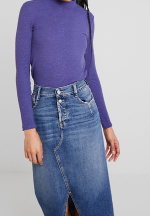 Lila gerippter Langarmtop, kombiniert mit einem hoch taillierten Jeansrock mit einem Schlitz vorne und zwei Knopfverschlüssen.